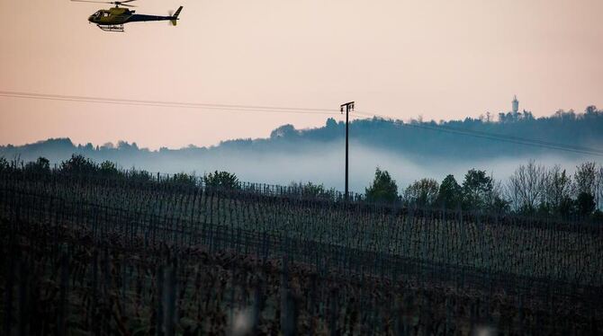 Ein Hubschrauber fliegt an einem Weinbaugebiet in Obersulm über Weinreben und versucht dabei mit tiefen Überflügen kalte und war