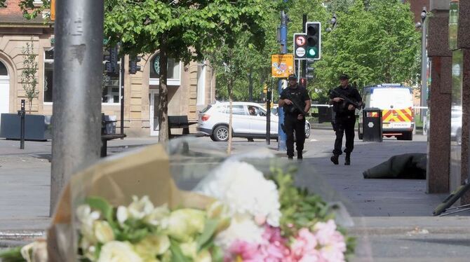 Bewaffnete Polizisten gehen in der Nähe der Manchester Arena in Manchester, im Vordergrund liegen Blumen auf dem Gehweg.