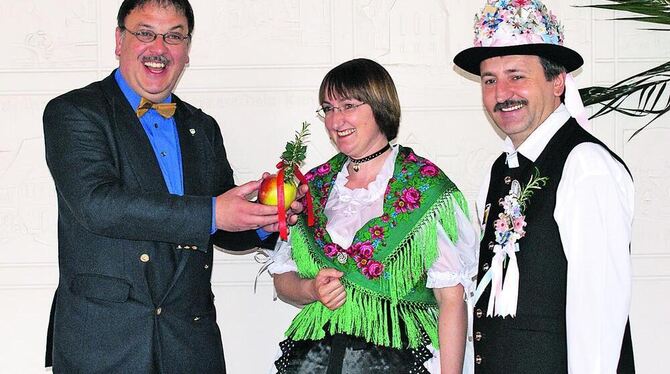 Das Trachtenpaar Eveline und Oswald Wolf übergibt die Einladung, die traditionell ein mit Rosmarinsträußchen geschmückter Apfel