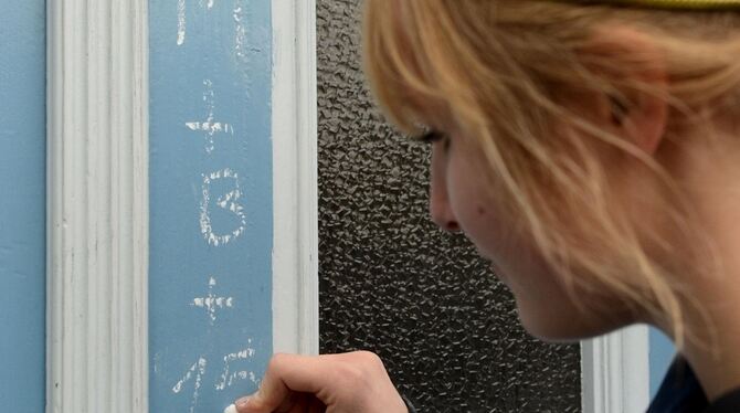 Eine Sternsingerin schreibt den Segensgruß an eine Haustür.  FOTO: DPA