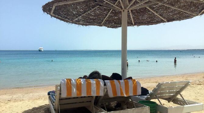 Eine Frau und ein Mann entspannen in Liegestühlen unter einem Sonnenschirm an einem öffentlichen Strand von Hurghada (Ägypten).