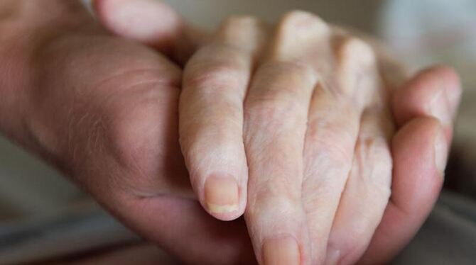 Ein Altenpfleger hält die Hand einer pflegebedürftigen Frau. Foto: Sebastian Kahnert/Illustration