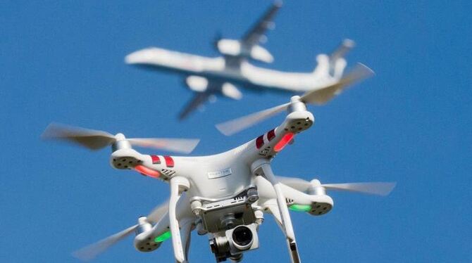 Eine private Drohne fliegt über einem Garten, während in einiger Entfernung ein Flugzeug beim zu sehen ist. Foto: Julian Stra
