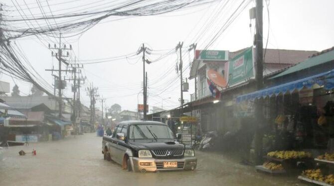 Ein Pkw steht auf Ko Samui im Dauerregen auf einer überfluteten Straße. Die ungewöhnlich heftigen Regenfälle haben auch die T