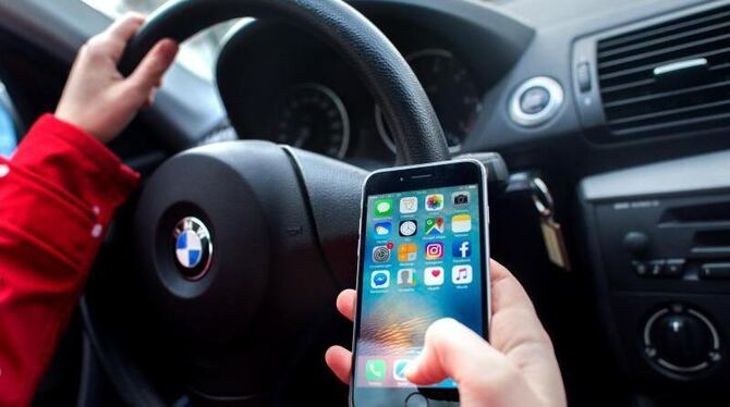Eine junge Frau sitzt am Steuer und bedient dabei ihr Smartphone. Foto: Hauke-Christian Dittrich