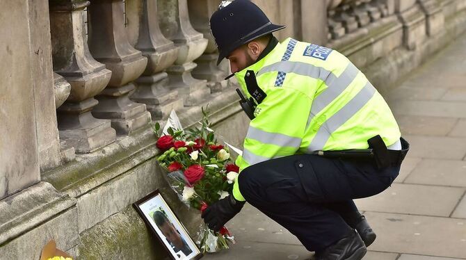 Ein Polizist legt Blumen an einem Foto in der Nähe des britischen Parlament in London nieder.