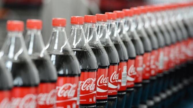 Flaschen mit Coca-Cola auf einem Transportband. Der Zuckeranteil des Getränks soll verringert werden. Foto: Jens Kalaene