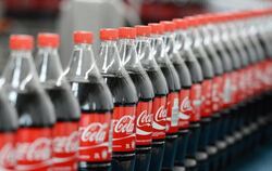 Flaschen mit Coca-Cola auf einem Transportband. Der Zuckeranteil des Getränks soll verringert werden. Foto: Jens Kalaene