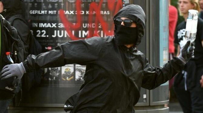 Ein maskierter Demonstrant wirft eine Flasche auf Polizeikräfte in Hamburg. Die Union fordert eine "europäische Extremistenda