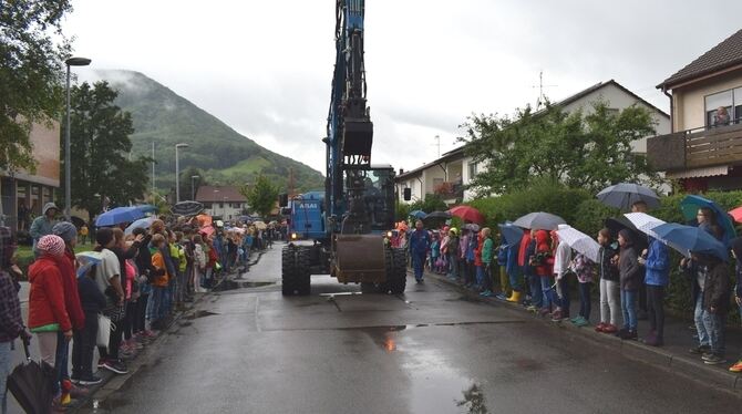 Rechts und links der Straße stehen Schüler im Regen und erwarten den Bagger, der den symbolischen Auftakt des 15 Millionen Euro