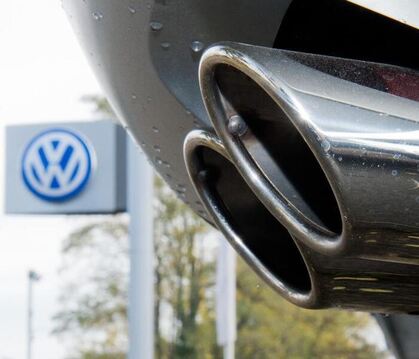 Der Auspuff eines Autos vor dem Schild eines VW-Händler. Foto: Julian Stratenschulte