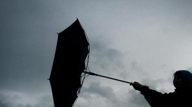 Von einer Windböe erfasst wird der Regenschirm eines Spaziergängers. Foto: Karl-Josef Hildenbrand/Illustration