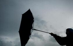 Von einer Windböe erfasst wird der Regenschirm eines Spaziergängers. Foto: Karl-Josef Hildenbrand/Illustration