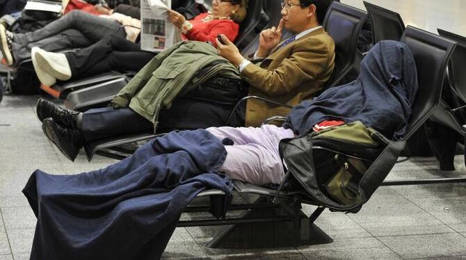 Von Kopf bis Fuß in Decken gewickelt warten gestrandete Passagiere auf eine mögliche Wiederaufnahme des Flugverkehrs.