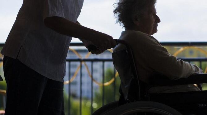 Eine Mitarbeiterin eines Seniorenheimes schiebt eine ältere Frau im Rollstuhl.