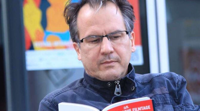 Der Festivalleiter der Französischen Filmtage Tübingen, Christopher Buchholz, posiert für den Fotografen mit einem Programmheft.