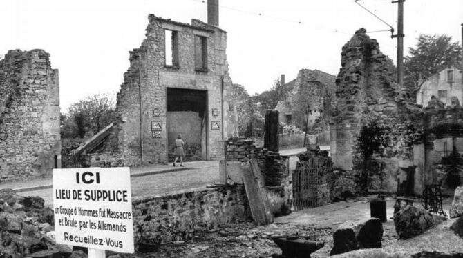 Blick auf die Ruinen von Oradour-sur-Glane (Frankreich) und eine Gedenktafel, deren Text lautet:"Gedenkstätte - Eine Gruppe v