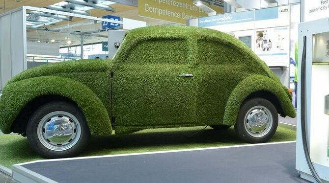 Ein mit Kunstrasen überzogener Volkswagen Käfer neben einer Ladesäule für Elektroautos auf der Hannover Messe. Laut Experten