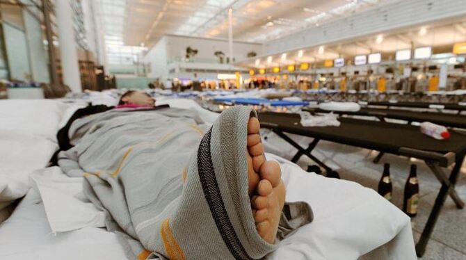 Ein Mann schläft auf einem Feldbett in der Schalterhalle des Münchner Flughafens. Foto: Tobias Hase