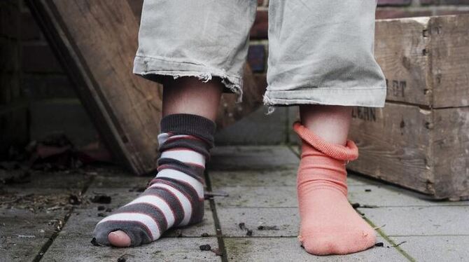 Ein Mädchen steht in abgetragener Kleidung ohne Schuhe in einem Hinterhof.