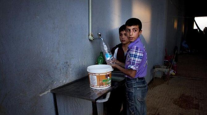 Zwei Jungen füllen in einem Flüchtlingslager an der syrisch-türkischen Grenze Wasser ab. Foto: Maysun / Archiv