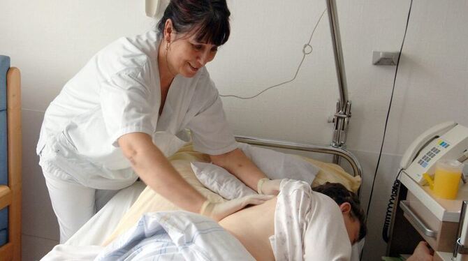 Die Pflegerin Roswitha Seeger reibt am einer Patientin im Universitätsklinikum Tübingen den Rücken ein. Seit Jahren klagen die K