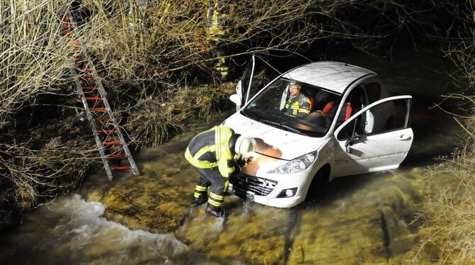 Ofterdinger Feuerwehrmänner sichern das in die Steinlach gefahrene Auto für die Bergung mit dem Autokran. GEA-FOTO: MEYER