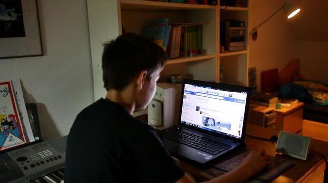 Ein Junge liest in seinem Kinderzimmer Facebook-Einträge. Foto: Oliver Berg