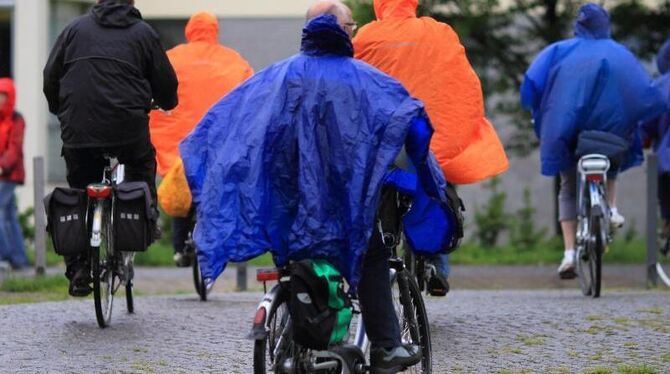 Radfahrer schützen sich mit Regenponchos vor den anhaltenden Niederschlägen. Foto: Jens Wolf