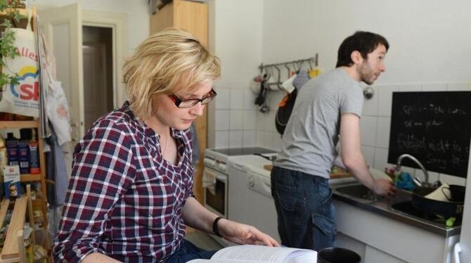 Ein Mann erledigt den Abwasch, während eine Frau ein Buch liest: 64 Prozent Männer finden einer Umfrage zufolge, dass es mit