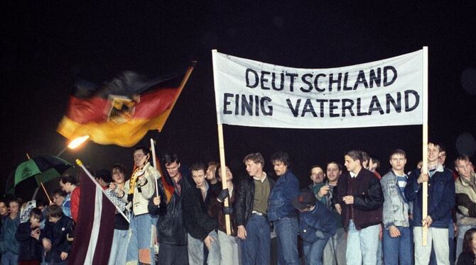 Mit der Deutschlandfahne und einem Transparent »Deutschland einig Vaterland« stehen Berliner am 1989 auf der Berliner Mauer am B