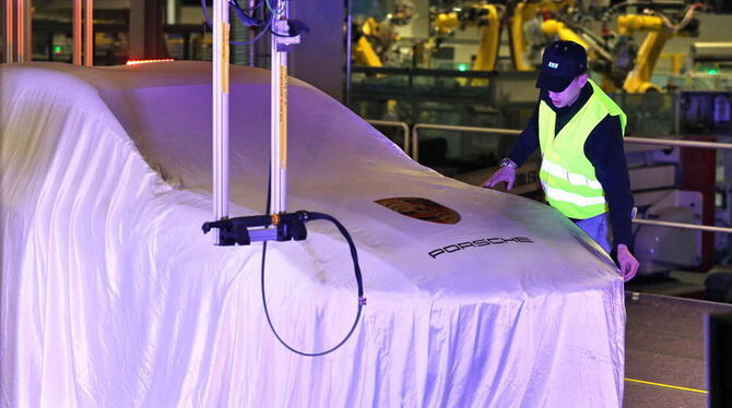 Ein Mann richtet das Tuch über einem verhüllten Porsche Macan in der neuen Karosseriefertigung des Sportwagenbauers in Leipzig.