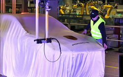 Ein Mann richtet das Tuch über einem verhüllten Porsche Macan in der neuen Karosseriefertigung des Sportwagenbauers in Leipzig.
