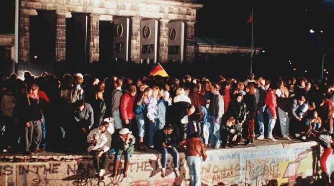 Jubelnde Menschen stehen am 09.11.1989 auf der Berliner Mauer vor dem Brandenburger Tor. Foto: dpa