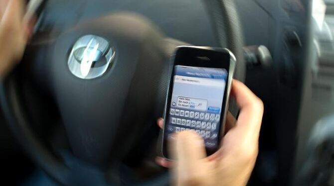 Eine Frau schreibt in einem Auto eine »SMS« auf ihrem Mobiltelefon. Foto: Arno Burgi