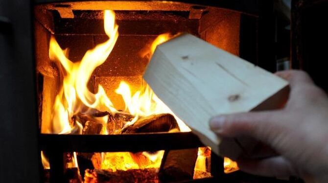 Ein Mann steckt Holz in einen Ofen.