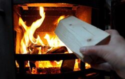 Ein Mann steckt Holz in einen Ofen.
