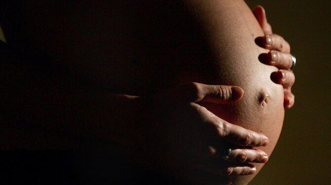 Eine schwangere Frau hält ihren Bauch in den Händen.