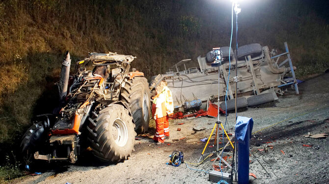 Rettungskräfte stehen neben einem verunfallten Traktor und einem doppelachsigen Anhänger an der Autobahn 8 (A8). Ein Traktorfahr