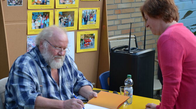 Günther Weber, Bäcker auf dem Lorettohof in Zwiefalten, signiert sein Buch im Hof der Burgwegschule.  FOTO: SAUTTER