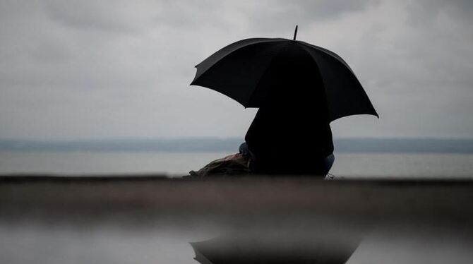 Eine Frau sitzt bei verregnetem Wetter unter einem Regenschirm
