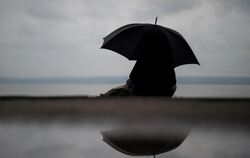 Eine Frau sitzt bei verregnetem Wetter unter einem Regenschirm