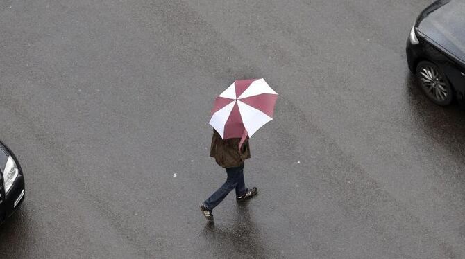 Ein Passant überquert mit einem Regenschirm eine Straße