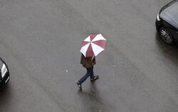 Ein Passant überquert mit einem Regenschirm eine Straße
