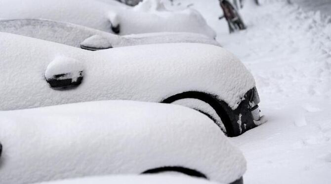 Eingeschneite Autos stehen am Straßenrand.