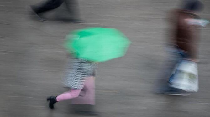Passantin geht mit ihrem Regenschirm eine Straße entlang