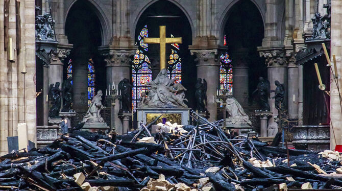 Trümmerteile und verkohlte Holzbalken im Inneren der Kathedrale Notre-Dame vor dem goldenen Kreuz.  FOTO: DPA