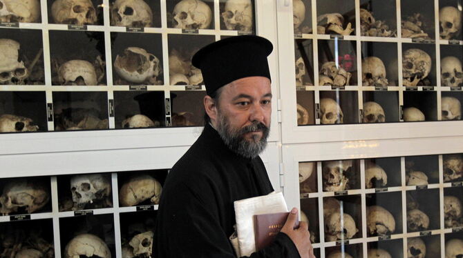 Ein griechischer Priester vor den Totenschädeln der Opfer des Massakers von Distomo.  FOTO: DPA