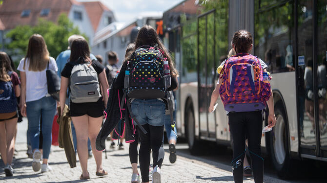 Schülerinnen gehen an einer Bushaltestelle in der Innenstadt zu stehenden Bussen.
