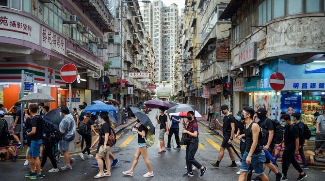 17.08.2019, China, Hongkong: Teilnehmer eines Protestmarsches laufen durch den Hongkonger Stadtteil Kowloon und schützen sich mi